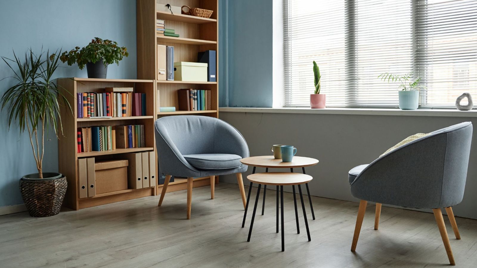 Duas poltronas, mesa de apoio e estante de livros junto a uma janela com luz natural